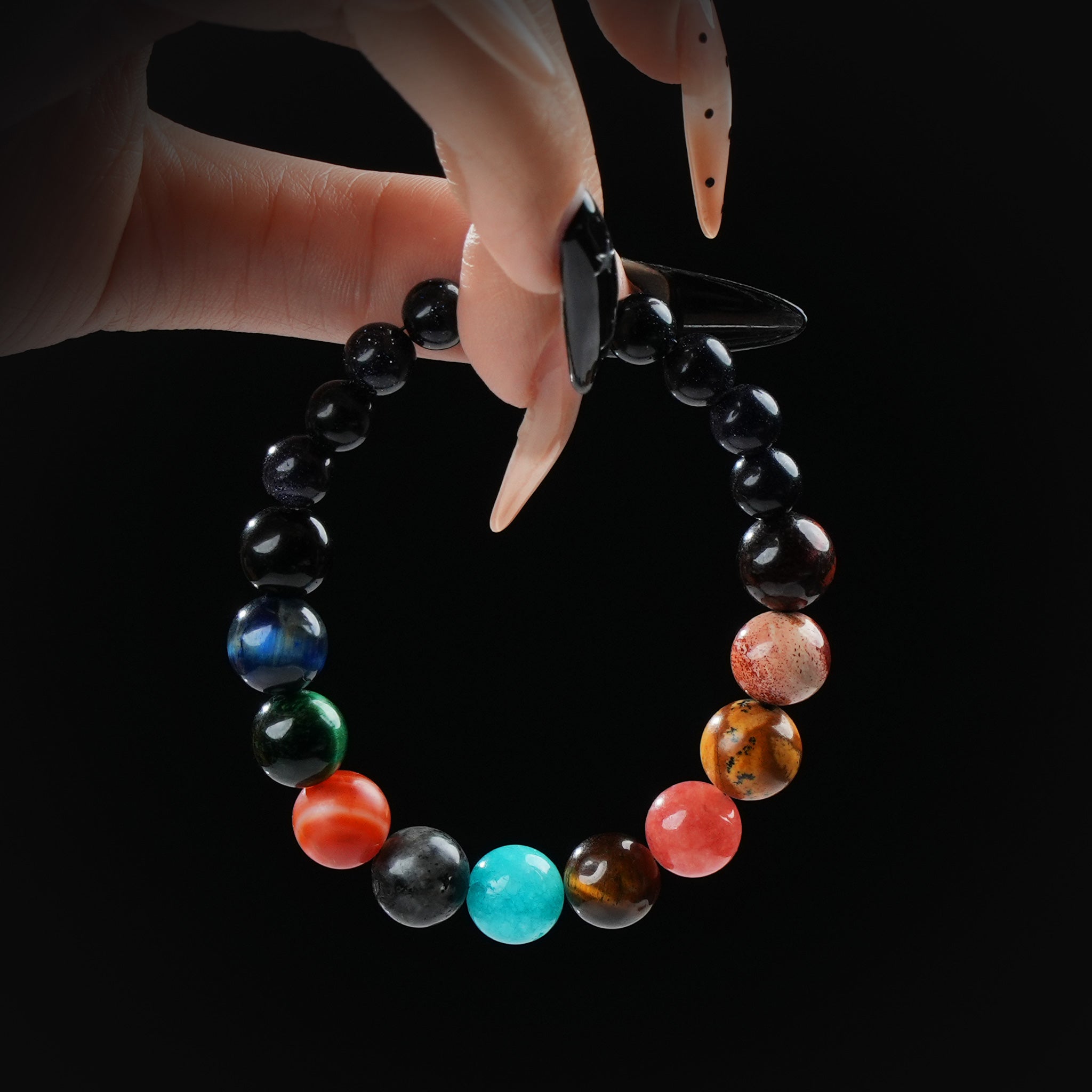 Bracelet made of multicolored gemstone beads representing the chakra colors, held by hand on a black background.