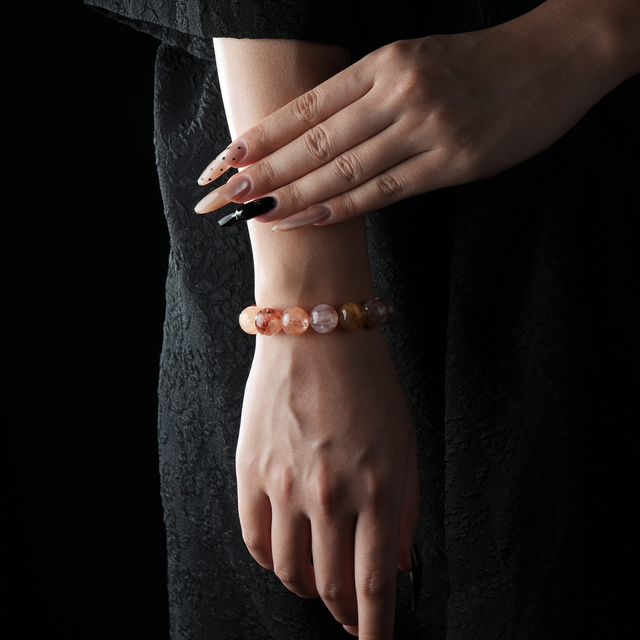 Bracelet made of polished red rutilated quartz beads, featuring vibrant reddish inclusions, worn on a wrist against a dark lace background.