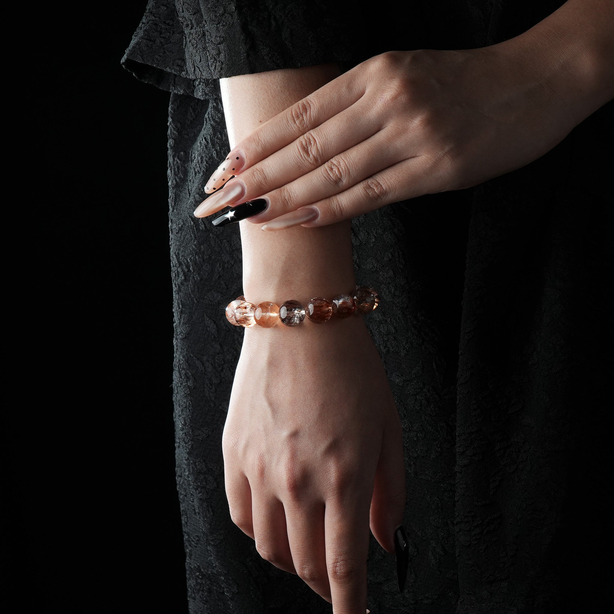 Bracelet made of red rutilated quartz beads, featuring deep reddish-brown threads within translucent stones, worn on a wrist with a black textured background.