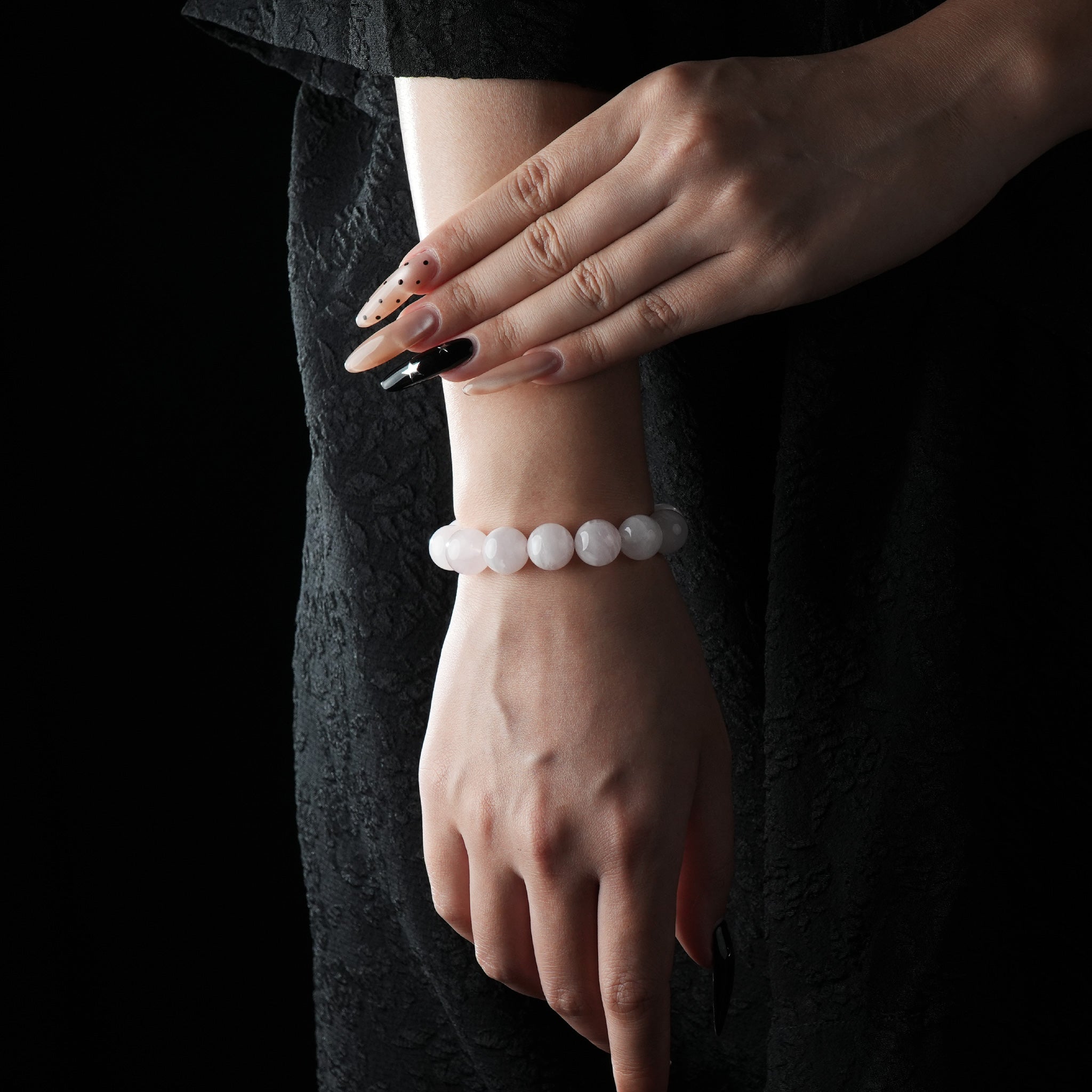 Delicate bracelet made of smooth, round rose quartz beads, worn on wrist with a black lace dress background.