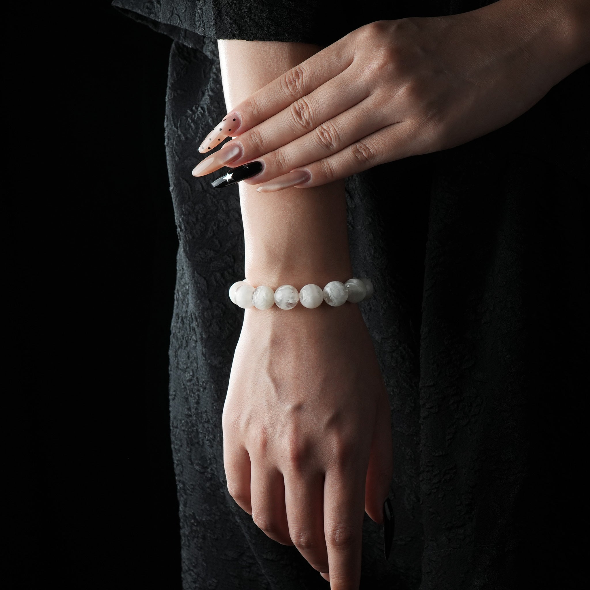 Elegant bracelet made of smooth, round snow phantom quartz beads, displayed on a wrist with a dark textured dress background.