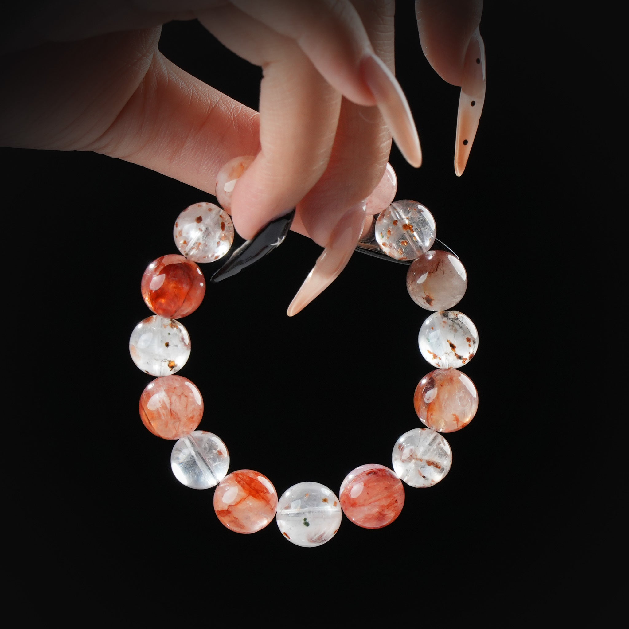 Strawberry quartz and lepidocrocite beaded bracelet with natural inclusions, held by hand on black background for love and emotional healing.
