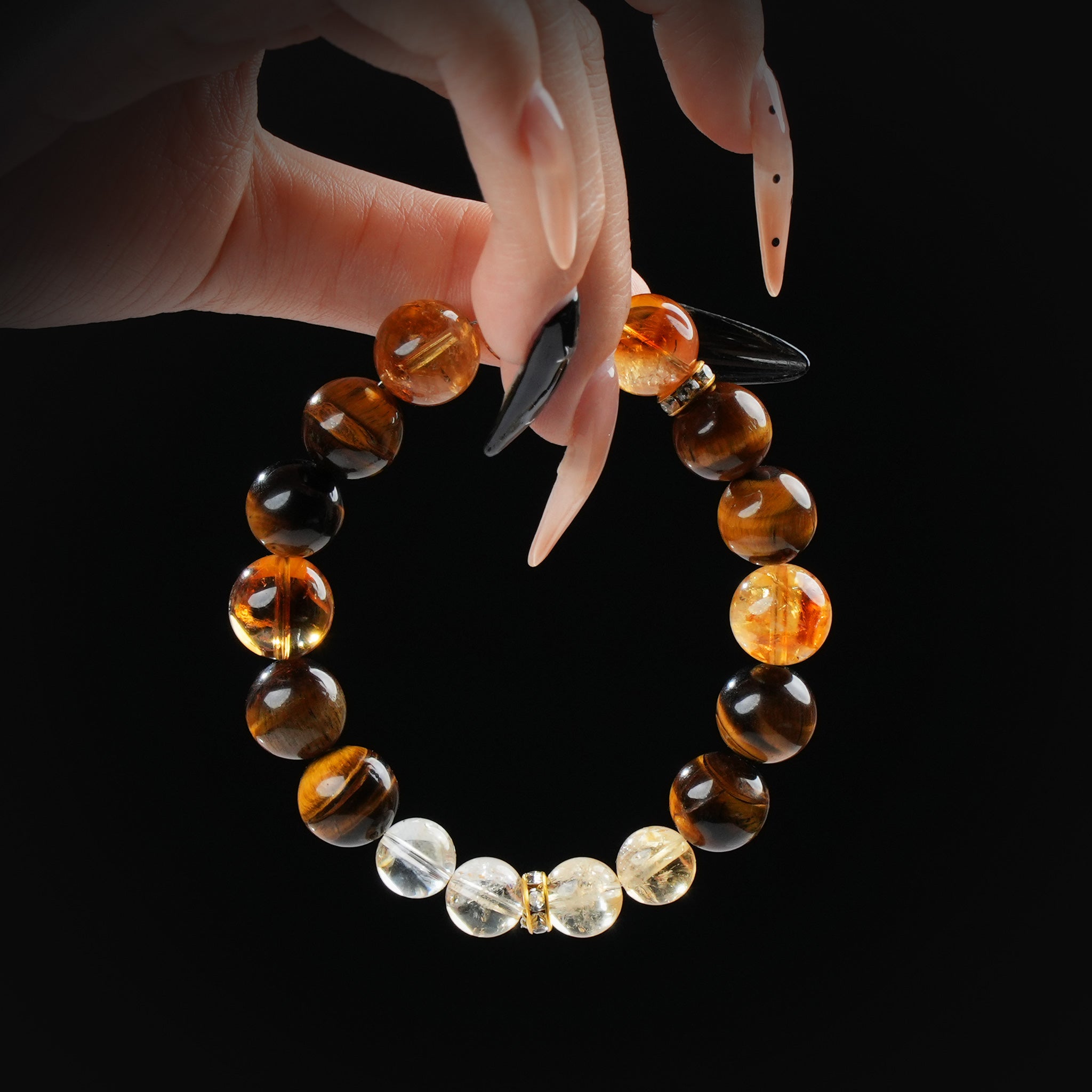 Tiger's eye, citrine, and clear quartz beaded bracelet held by hand on black background for confidence and abundance.