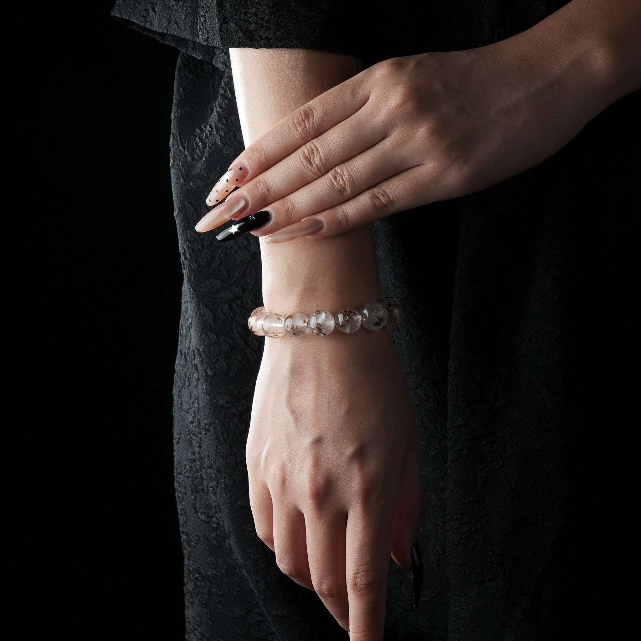 Elegant bracelet made of round white phantom quartz beads with natural mineral inclusions, worn on wrist against a black dress background.
