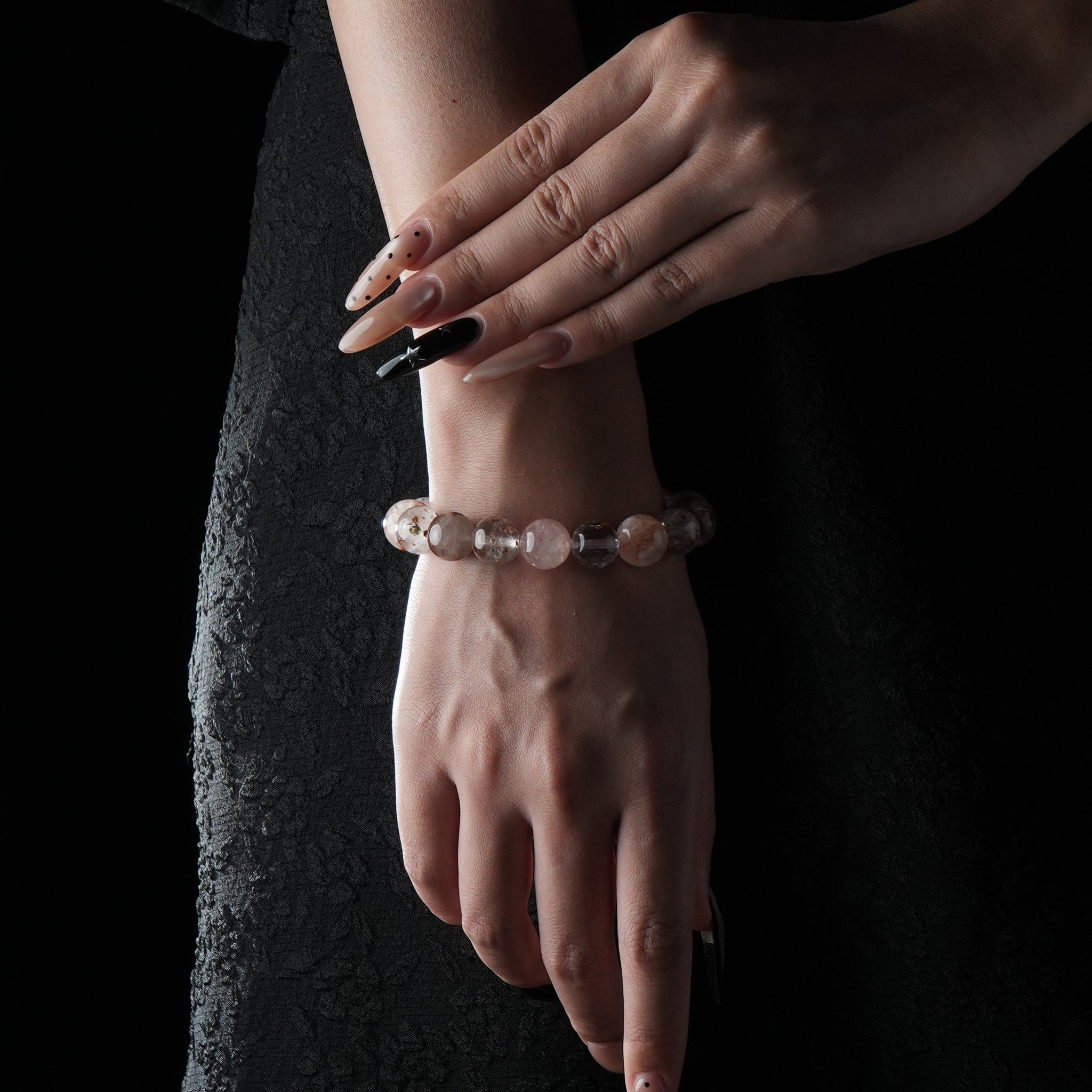 Delicate bracelet featuring white phantom quartz and strawberry quartz beads, worn on wrist with a dark fabric background.
