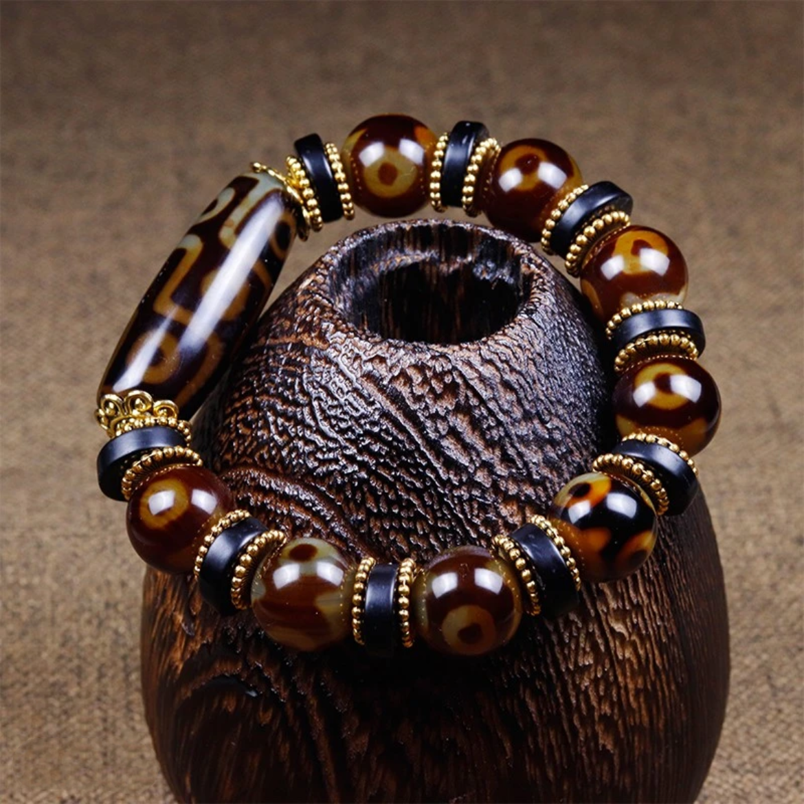This photograph presents the bracelet draped around a carved wooden display piece, emphasizing its cultural charm. The Dzi bead's patterns are clearly visible, and the warm tones of the agate beads contrast beautifully with the dark wood texture, enhancing the bracelet’s artisanal quality and grounding spiritual presence.