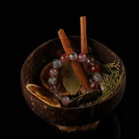 Top view of a bracelet surrounded by bay leaves, herbs, and cinnamon sticks in a rustic coconut bowl.