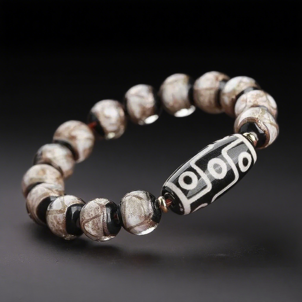 A minimalistic Dzi bracelet showcasing a black and white 9-eye bead at the center, framed by matte beige and brown beads with abstract patterns. The texture and soft glow of the materials reflect a more grounded, earthy spiritual energy.