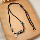 The Tibetan 9-eye agate Dzi bead necklace, featuring gold and gemstone accents, laid flat on a wooden surface, showcasing its cultural and spiritual significance.
