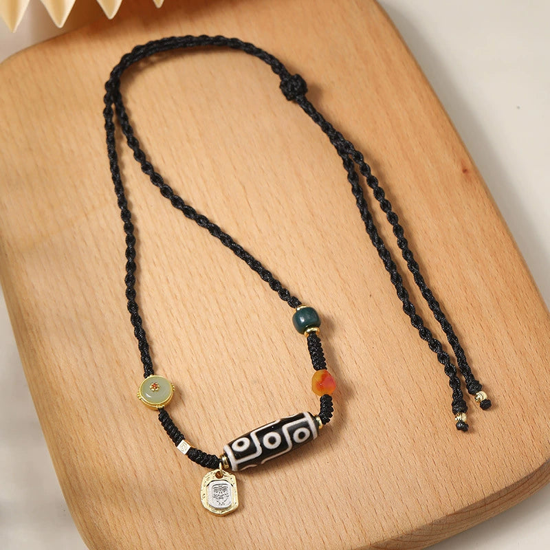 The Tibetan 9-eye agate Dzi bead necklace, featuring gold and gemstone accents, laid flat on a wooden surface, showcasing its cultural and spiritual significance.