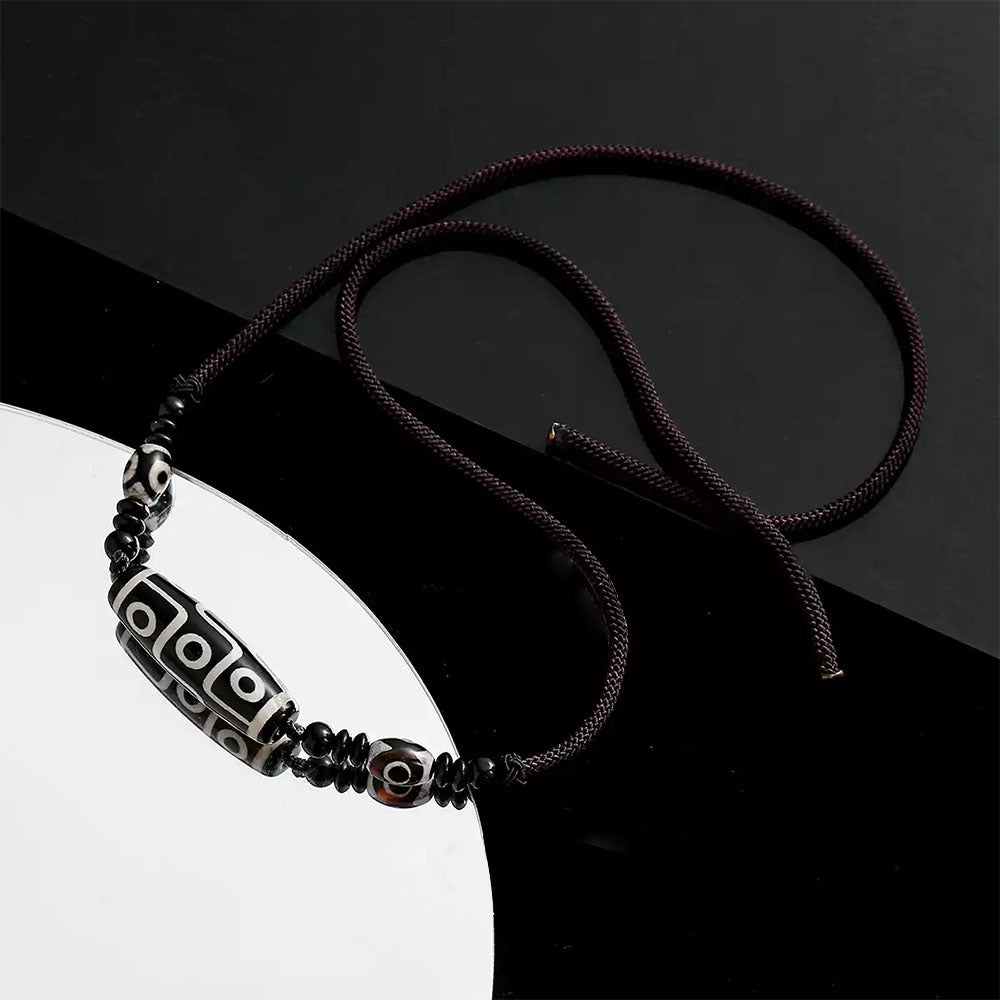 The Tibetan Nine-Eyed Dzi bead necklace rests on a reflective black surface, highlighting the polished beads and their distinct patterns.