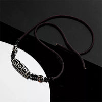 The Tibetan Nine-Eyed Dzi bead necklace rests on a reflective black surface, highlighting the polished beads and their distinct patterns.