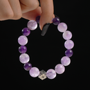 This gemstone bracelet features alternating hues of soft lavender and rich violet Amethyst beads, centered around a detailed silver cube charm. The harmonious gradient of purples exudes elegance and tranquility. Shown suspended between fingers, the bracelet gleams subtly against a dark backdrop, emphasizing its polished finish and the intricate design of the silver charm.