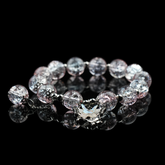 A bracelet of soft pink and clear crackled beads, sweet and gentle in tone, accented with a shimmering butterfly charm at its center.