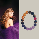 A side-by-side composition: on the left, a glamorous woman with wavy blonde hair looks over her shoulder, wrapped in soft layers of purple tulle. On the right, a gemstone bracelet composed of amethyst, tiger eye, and garnet beads is displayed in a circular layout against a white background. The deep purples and warm golden tones of the bracelet subtly echo the elegance and color palette of the woman's ensemble.