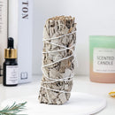 A close-up of a sage smudge stick with amethyst and palo santo, styled next to a lily essential oil bottle.