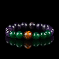 A vibrant gemstone bracelet featuring deep purple amethyst, vivid green agate, and a central polished tiger eye bead. The piece is showcased on a reflective black surface, highlighting the contrasting colors and natural luster of each stone.