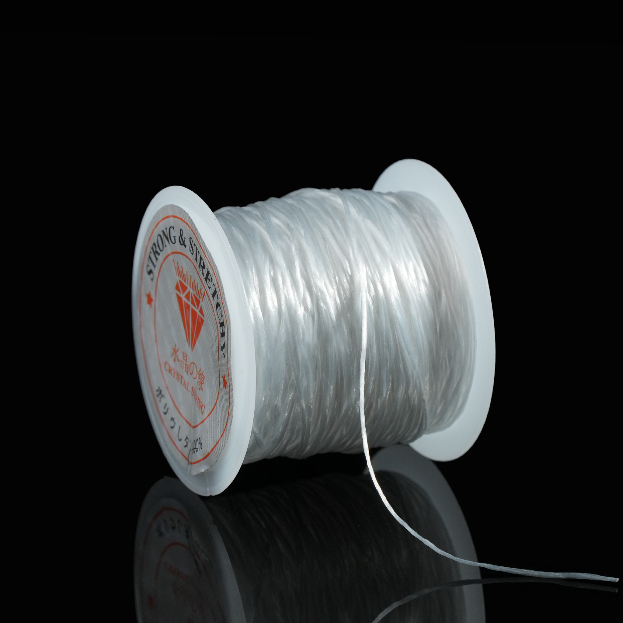An angled view highlighting the clean structure of the spool and the shine of the clear flat elastic thread. The high-contrast black background emphasizes the spool’s form and clarity.