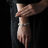 A delicate bracelet made of aquamarine, moonstone, and clear quartz beads, worn on the wrist against a black dress background.