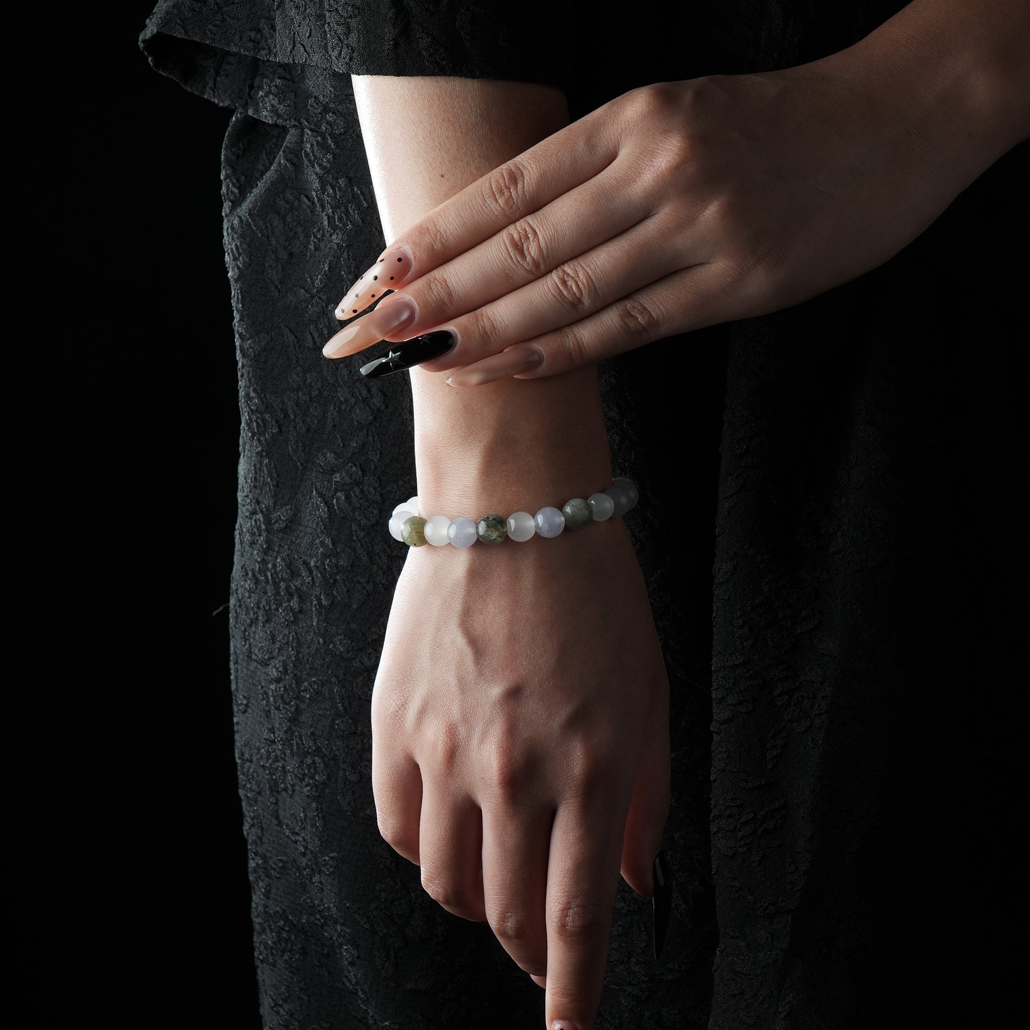 A delicate bracelet made of aquamarine, moonstone, and clear quartz beads, worn on the wrist against a black dress background.