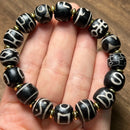 A handmade Tibetan-style bracelet featuring black round beads with white symbolic engravings, held in the palm of a hand. Each bead is separated by small gold-tone spacer beads, showcasing traditional artistry and cultural symbolism.