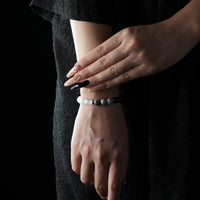 A minimalist bracelet featuring black obsidian and white cat’s eye beads, worn on the wrist with a black lace dress.