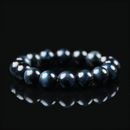 Close-up of a polished blue tiger eye bracelet placed on a black reflective surface, showcasing its deep navy sheen and layered chatoyancy under soft lighting.