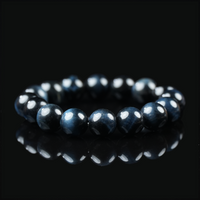 Close-up of a polished blue tiger eye bracelet placed on a black reflective surface, showcasing its deep navy sheen and layered chatoyancy under soft lighting.
