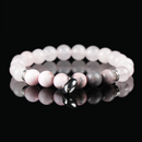 A close-up of a rose quartz and rhodonite beaded bracelet with a silver heart charm, placed on a reflective black surface.