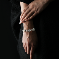 A woman's wrist wearing a white-toned crystal bracelet against a black outfit, featuring clear and rutilated quartz with subtle silver and blue accents.