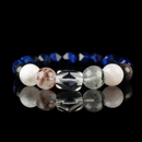 A gemstone bracelet featuring a central carved clear quartz bead, flanked by mica red rutilated quartz, snow phantom, silver obsidian, and faceted lapis lazuli beads. The arrangement of natural stones showcases a harmonious blend of translucent, earthy, and deep blue hues, set against a reflective black surface.