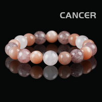 Flat lay of Cancer zodiac bracelet with strawberry quartz, white moonstone, and peach sunstone beads on black reflective background.