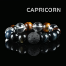 Flat lay of Capricorn zodiac crystal bracelet with tiger eye, obsidian, lava stone, and clear quartz beads on black reflective background.