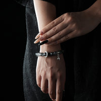A bracelet featuring celestial energy beads with a moon and feather charm, worn on a wrist against a black outfit.