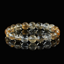 Close-up of a citrine bracelet composed of golden-yellow and clear translucent beads, arranged on a reflective black surface to highlight its radiant clarity and energetic glow.