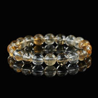 Close-up of a citrine bracelet composed of golden-yellow and clear translucent beads, arranged on a reflective black surface to highlight its radiant clarity and energetic glow.