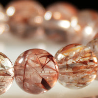 Macro shot of red rutilated quartz crystal beads showing internal needle-like rutile structures and polished surfaces.