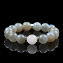 A high-resolution image of a rose quartz and gray moonstone bracelet with soft pink and shimmering gray beads arranged in a balanced design, displayed on a reflective black surface.