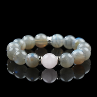 A high-resolution image of a rose quartz and gray moonstone bracelet with soft pink and shimmering gray beads arranged in a balanced design, displayed on a reflective black surface.