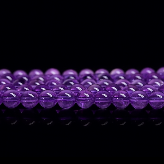 This image features a close-up view of multiple strands of polished deep purple crystal round beads, likely amethyst. The beads are arranged in neat rows on a glossy black surface, with a reflective finish that enhances their vibrant color and smooth texture.
