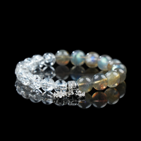 Close-up view of a bracelet made from shimmering grey moonstone and clear Himalayan quartz, adorned with silver snowflake and butterfly dangles.