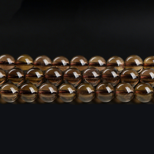 A close-up image showing multiple strands of polished smoky quartz round beads laid out horizontally. The beads display a translucent brown hue with a smooth, glossy surface and visible internal textures.