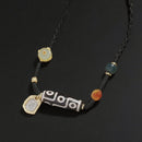 A close-up of the Tibetan 9-eye Dzi bead necklace laid flat, showing the black cord, the carved agate bead with a unique 9-eye pattern, and colorful gemstone beads with a gold charm.