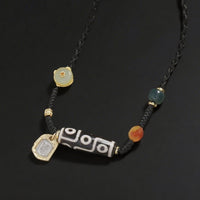 A close-up of the Tibetan 9-eye Dzi bead necklace laid flat, showing the black cord, the carved agate bead with a unique 9-eye pattern, and colorful gemstone beads with a gold charm.