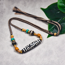 A detailed close-up of the Tibetan Nine-Eye Agate Dzi bead necklace with vibrant turquoise, black agate, and golden accents, placed on a gray surface to highlight the design.