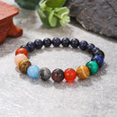 A planetary crystal bracelet placed on a rustic surface with greenery, showcasing polished gemstone beads.