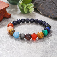 A planetary crystal bracelet placed on a rustic surface with greenery, showcasing polished gemstone beads.