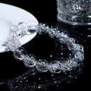 A Himalayan quartz bracelet displayed near a clear cup on a glossy black surface, reflecting vibrant light sparkles.