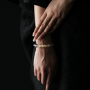 A woman’s wrist adorned with a luminous crystal bracelet featuring clear quartz, golden citrine, and silver-toned obsidian beads, shown against a black textured dress.