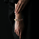 A woman's hand wearing a translucent crystal bracelet featuring hematoid quartz and clear quartz, photographed against a black outfit with soft lighting.